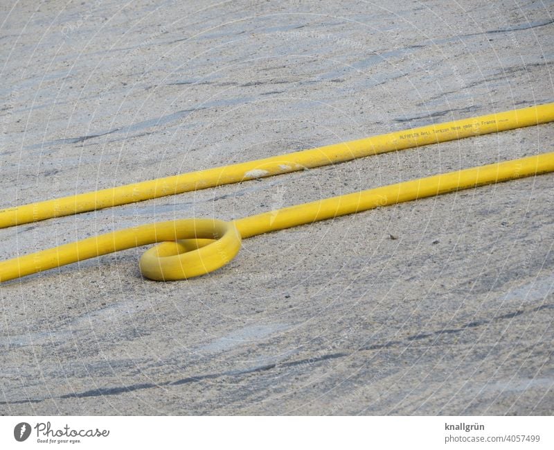 Gelber Wasserschlauch mit Looping Baustelle gelb Schlinge looping Schlauch Gartenschlauch Außenaufnahme Boden liegen nebeneinander parallel zwei rund grau