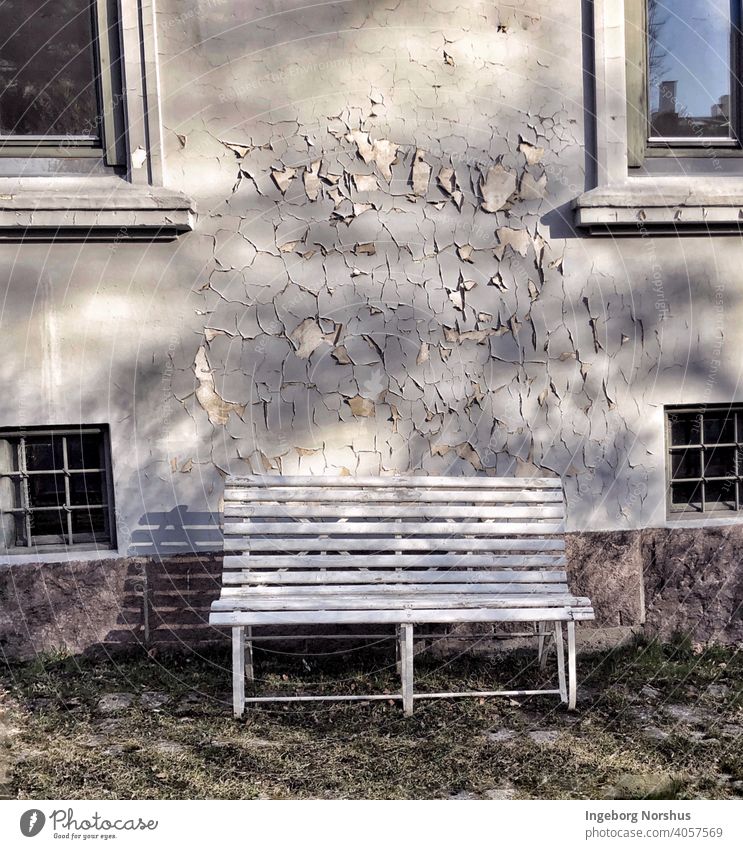 Eine Bank vor einer grauen Wand mit abblätternder Farbe Holzbank Farbfoto Menschenleer Außenaufnahme Tag Gedeckte Farben Einsamkeit Textfreiraum oben