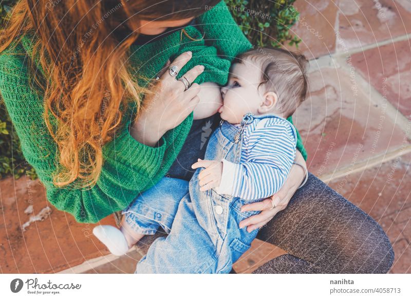 Junge Frau stillt ihr Baby im Freien an einem sonnigen Tag jung Mutter Mama Familie Stillen grün Feiertage Freizeit Gesundheit blond Pflege Kindheit