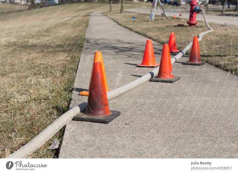 Feuerwehrschlauch, Hydrant und orangefarbene Verkehrsleitkegel; Aufbau für Hydrantenspülung in einer Nachbarschaft Straße Zapfen Asphalt Ermahnung Kegel Wasser