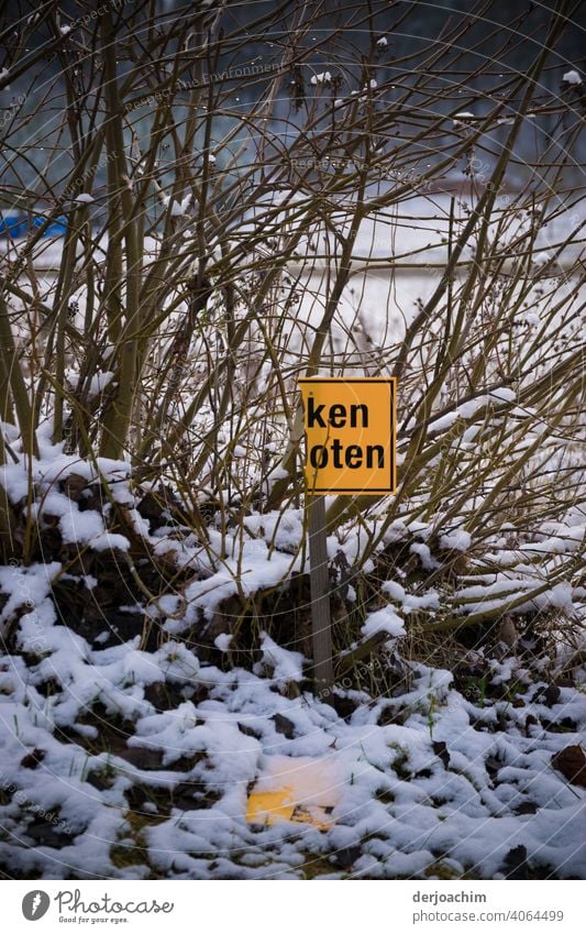 Halb abgerissenes Schild in einer Winterlandschaft . ken  oten. Der andere Teil liegt auf dem Boden .. Hinweisschild Außenaufnahme Buchstaben Nahaufnahme