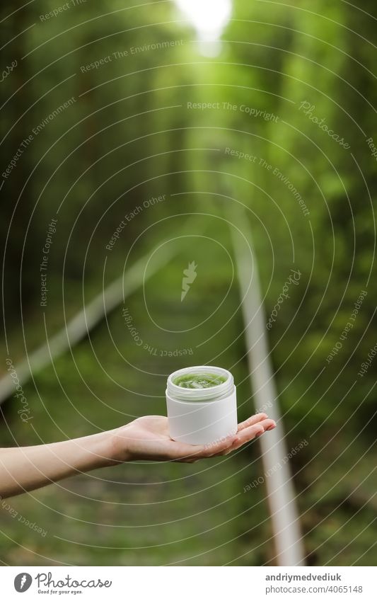 Junge weibliche Hand halten ein Glas grüne natürliche Creme für Gesicht oder Körper. organische natürliche Hautpflegeprodukte auf grünen natürlichen Hintergrund. Verpackung von Lotion oder Creme. Schönheit Kosmetik Hautpflege Konzept.