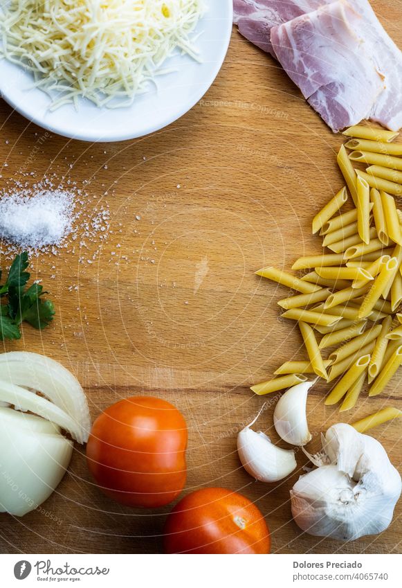 Zutatenliste zum Kochen von Makkaroni mit Tomate und Speck Tomaten Salatbeilage Knoblauch Zwiebeln Salz Holzplatte braun salzig Käse geschnitten Essen