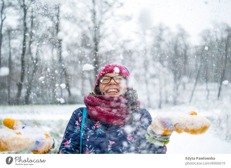 Frau wirft Schnee in die Luft und genießt einen kalten Wintertag Werfen Brille außerhalb natürlich Gesundheit Fausthandschuh Schal Bäume Handschuhe Schneeflocke