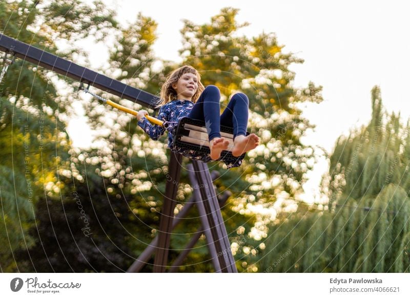 Kleines Mädchen spielt auf der Schaukel im Park Kind pendeln spielerisch barfuß Aktion Freizeitaktivitäten Aufregung Spielen Kleid Frühling Freiheit Tag