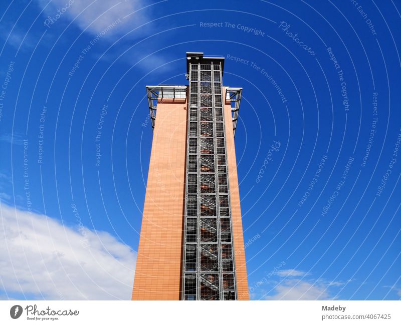 Außenliegende Stahlkonstruktion einer Feuertreppe an der Fassade eines Hochhaus in leuchtendem Orange vor blauem Himmel im Sonnenschein in Frankfurt am Main Fechenheim in Deutschland