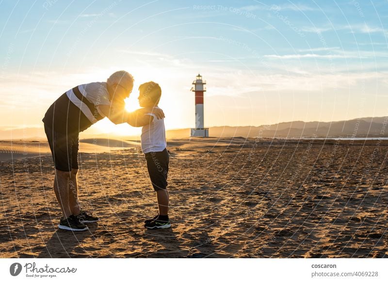 Großvater und Enkel umarmen sich an einem Strand mit einem Leuchtturm im Hintergrund Rücken Junge Kind Kindheit Kinder Küste Papa Tag älter Familie Fangar