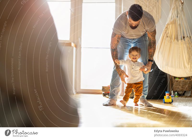 Kleiner Junge lernt laufen mit seinem Vater neben ihm zu Hause alleinerziehend alleinerziehender Vater Vatertag Vaterschaft zu Hause bleiben Dad