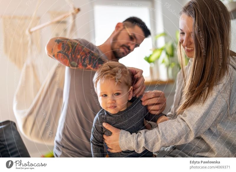 Junges Paar kleidet ihren kleinen Sohn zu Hause Familie Vater Kind Mädchen bezaubernd Kleinkind Kindererziehung Raum Tochter Appartement gutaussehend Spielen