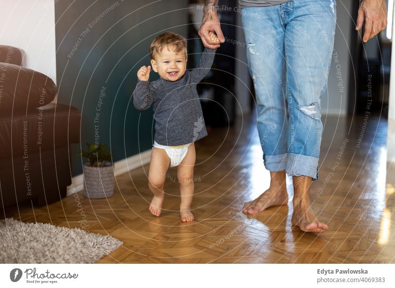 Kleiner Junge lernt laufen mit seinem Vater neben ihm zu Hause alleinerziehend alleinerziehender Vater Vatertag Vaterschaft zu Hause bleiben Dad