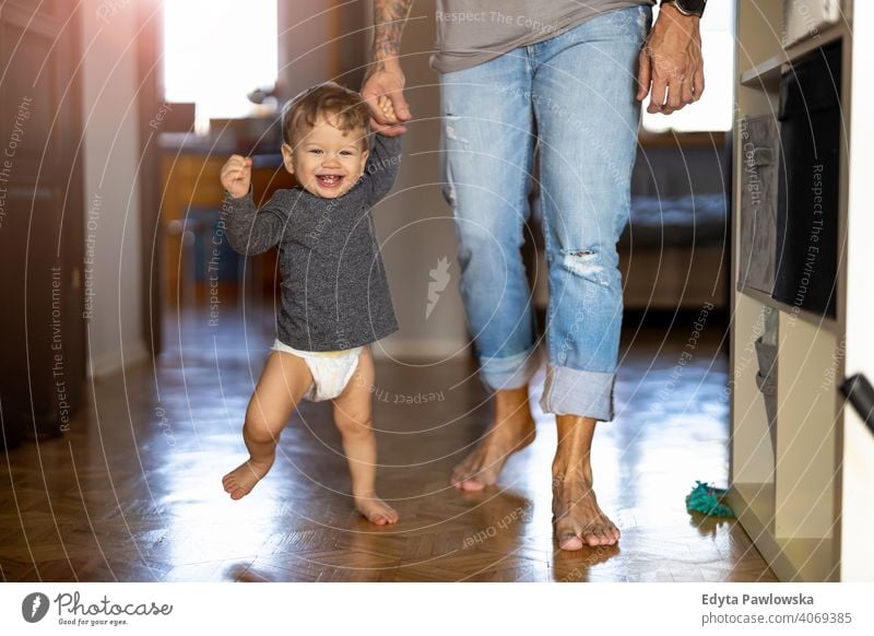 Kleiner Junge lernt laufen mit seinem Vater neben ihm zu Hause alleinerziehend alleinerziehender Vater Vatertag Vaterschaft zu Hause bleiben Dad