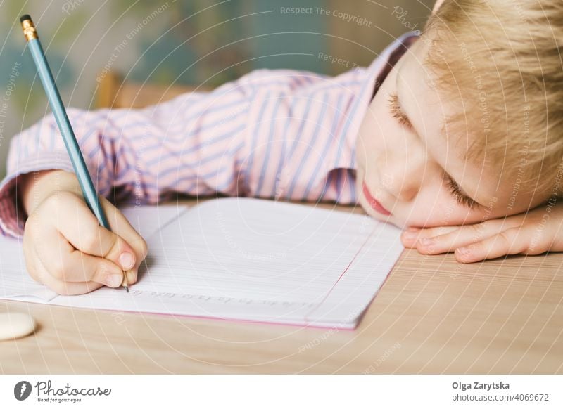 Kind schreibt in ein Notizbuch und liegt auf dem Schreibtisch. Junge lernen schreibend wenig müde schlafen Tun niedlich blond rosa Hemd Bleistift