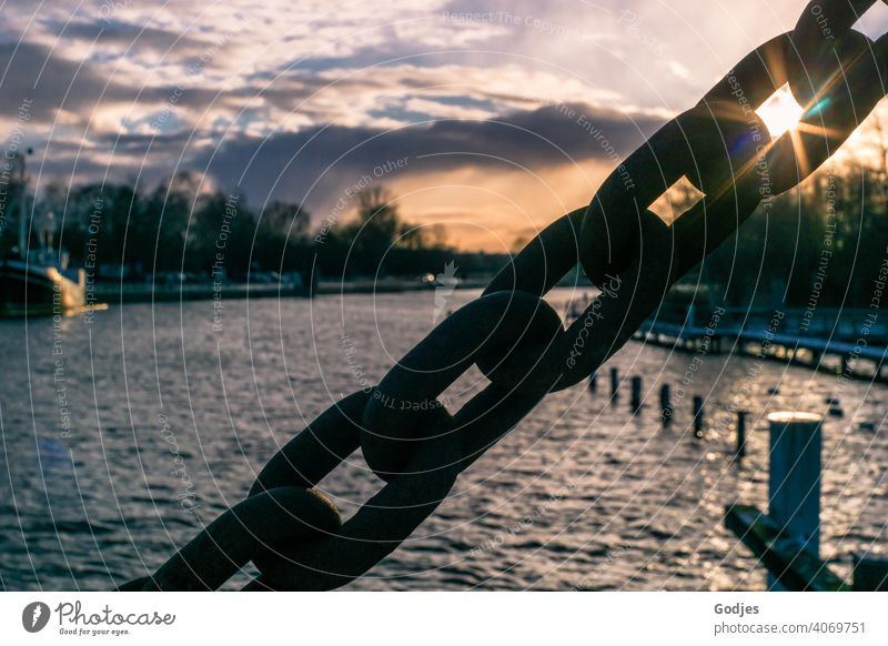 Sonne scheint durch das Glied einer massiven Stahlkette gegen den bewölkten Himmel der Abenddämmerung über dem Fluss anketten Kettenglieder Sonnenstrahlen