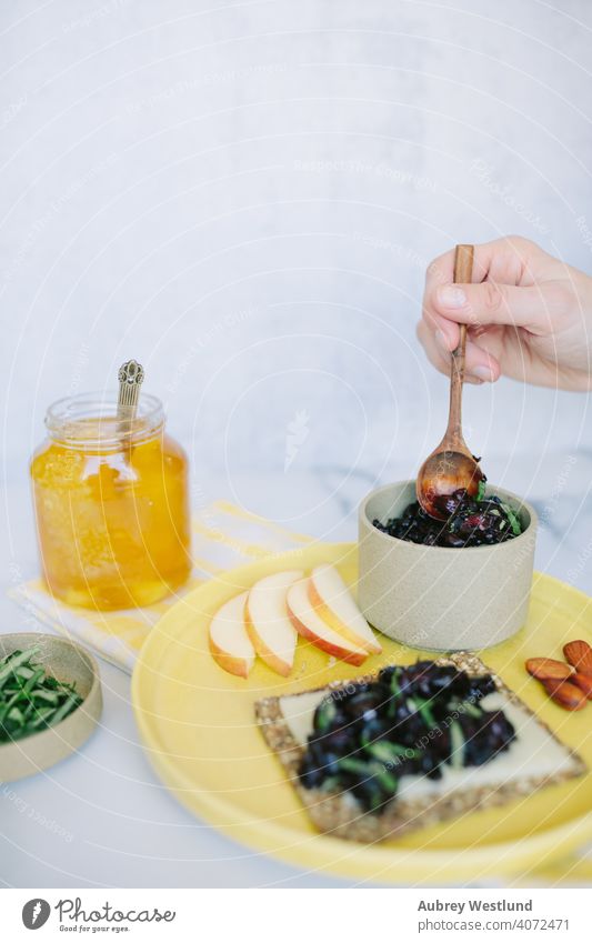 Frau bei der Zubereitung eines Sommersnacks mit Kirsch-Relish auf einem Körnercracker Mandeln Amuse-Gueule Vorspeisen Äpfel Sortiment Hintergrund Basilikum