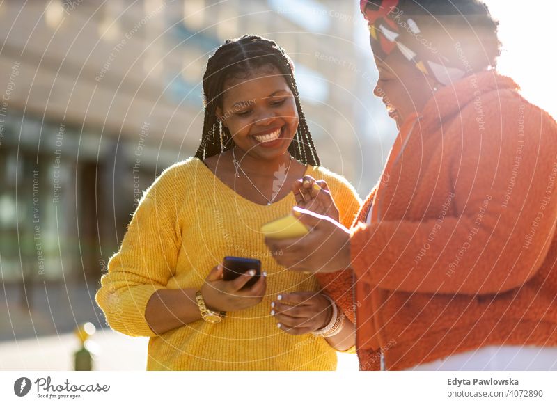 Glückliche Freundinnen, die mit ihren Smartphones in der Stadt Nachrichten versenden Vielfalt unterschiedliche Menschen Liebe im Freien Tag Positivität