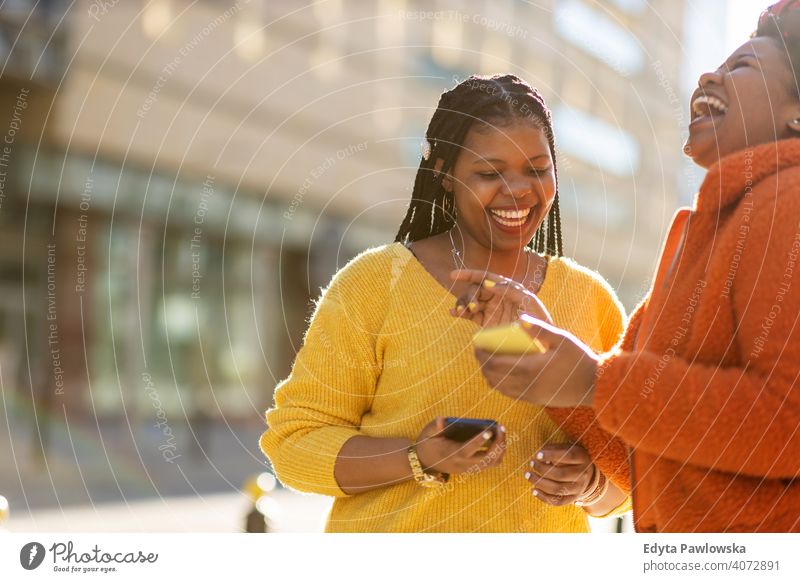 Glückliche Freundinnen, die mit ihren Smartphones in der Stadt Nachrichten versenden Vielfalt unterschiedliche Menschen Liebe im Freien Tag Positivität