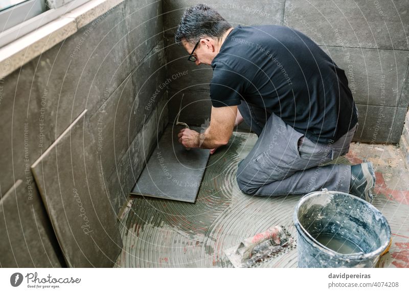 Handwerker beim Verlegen von Fliesen auf einer Terrasse Maurer Reform Verlegung Fliesen u. Kacheln leichte Stöße Spachtel Wasserhahn verglaste Terrasse