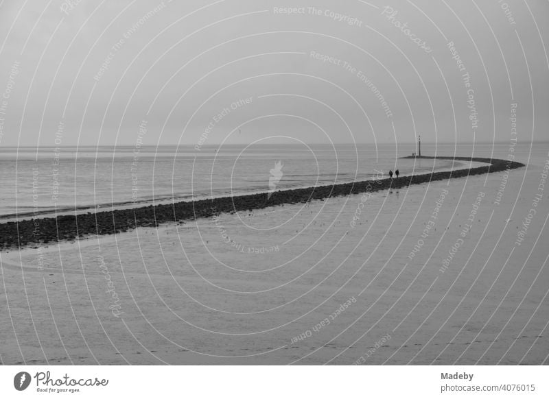 Spaziergänger auf der Hafenmole bei Regenwetter in Norddeich an der Küste der Nordsee in Ostfriesland in Niedersachsen, fotografiert in klassischem Schwarzweiß