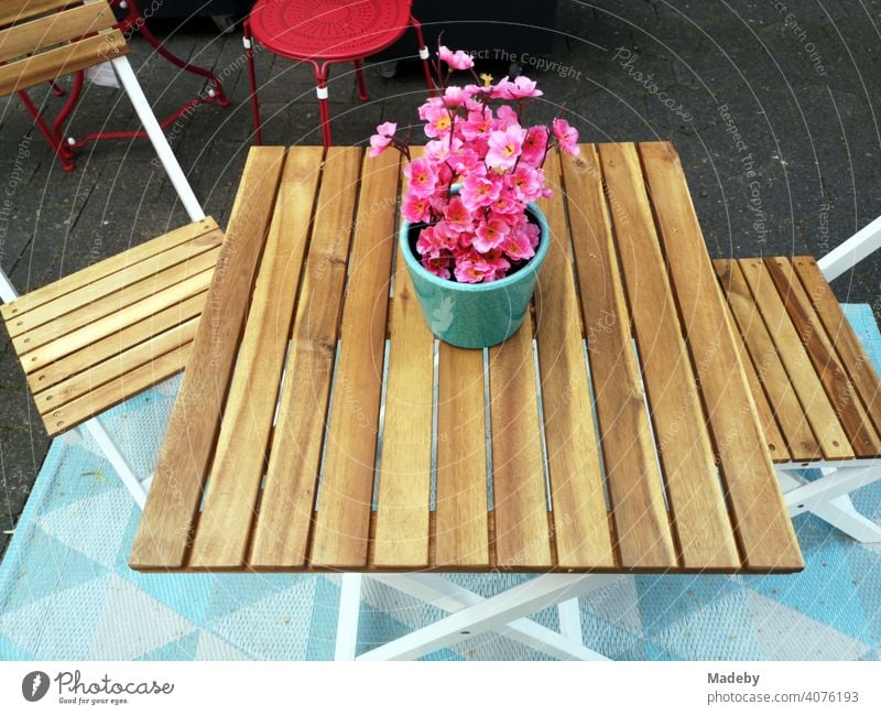 Gartentisch aus hellem Holz mit Bistrostühlen mit Blumentopf mit Pflanze mit rosa Blüten vor einem Geschäft in der Altstadt von Detmold in Ostwestfalen-Lippe