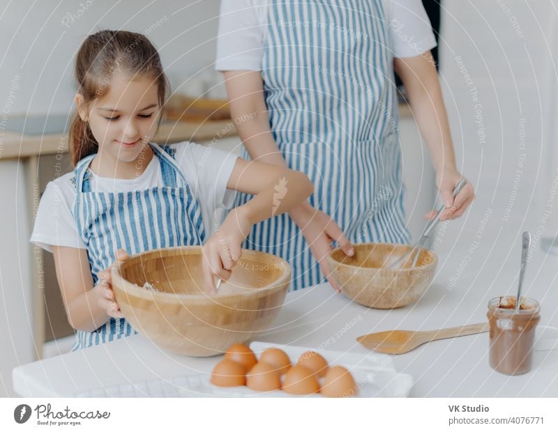 Mutter gibt kleinen Kind kulinarische Lektion, stehen nebeneinander, mischen Zutat in großen Holzschüsseln, machen Teig zusammen, verwenden Eier, Mehl und andere Produkte. Familie, Kochen, Mutterschaft