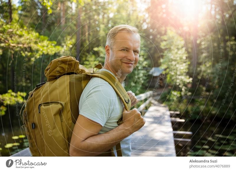 Reifer Mann erkundet die finnische Natur im Sommer, geht über die Brücke. Wanderer mit großen Rucksack Reisen in Wäldern. Sommer skandinavischen Landschaft von Seen und Wäldern.