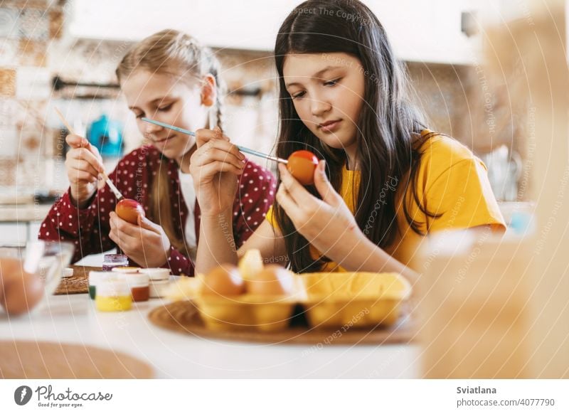 Zwei Schwestern sitzen am Tisch und malen Ostereier in verschiedenen Farben für Ostern Frühling Kind Feiertag Vorbereitung Ei hell Familie Mädchen weiß