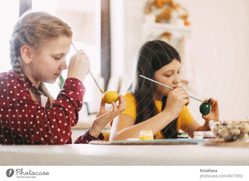 Zwei Schwestern sitzen am Tisch und bemalen Ostereier in verschiedenen Farben für Ostern, Nahaufnahme Frühling Kind Feiertag Vorbereitung Ei hell Familie