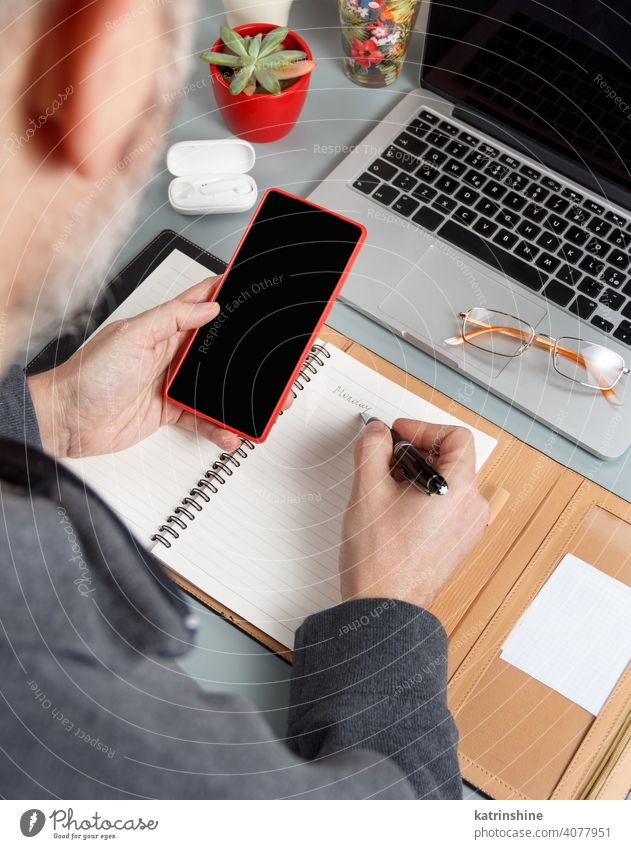 Mann schreibt MONTAG in Agenda und benutzt Handy auf einem grauen Bürotisch Nahaufnahme Business Hände schreiben intelligentes Arbeiten Laptop Planer