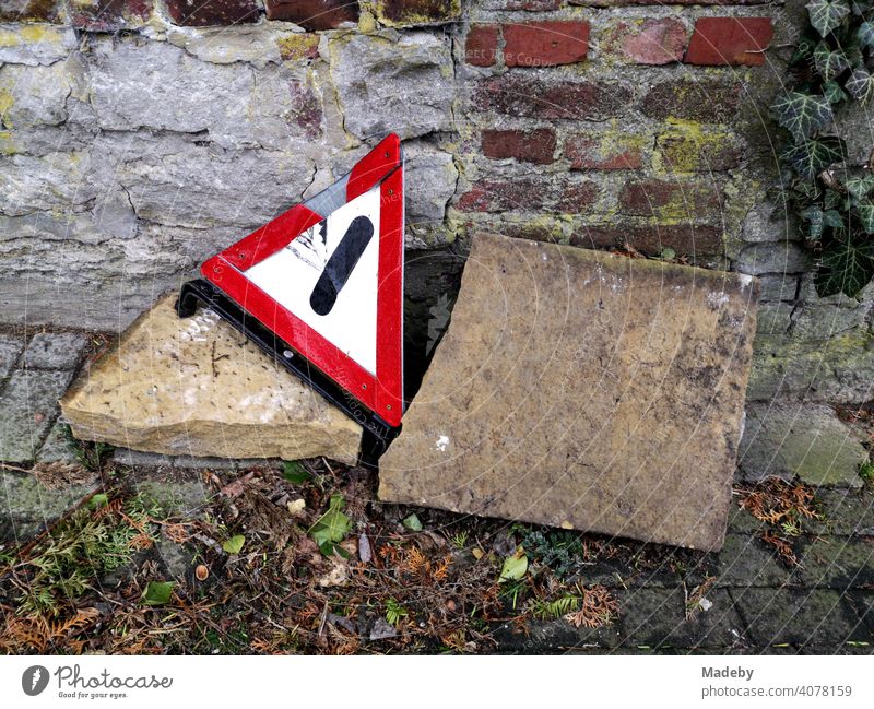 Altes kaputtes Warndreieck auf großen Steinen am Straßenrand auf Kopfsteinpflaster vor Mauerwerk im Herbst in der Altstadt von Oerlinghausen bei Bielefeld im Teutoburger Wald in Ostwestfalen-Lippe