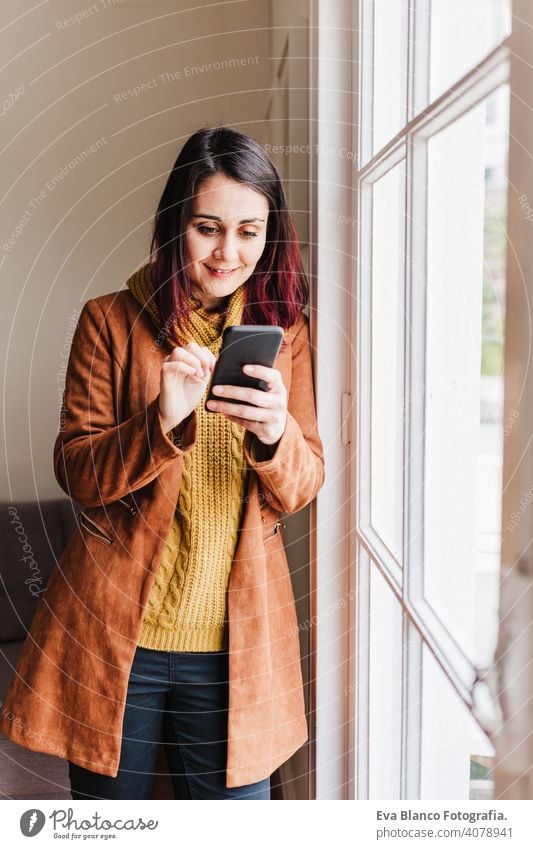 Junge schöne Frau zu Hause mit Handy am Fenster. Technologie und Lebensstil heimwärts Technik & Technologie Heimarbeitsplatz Kaukasier Freizeitkleidung