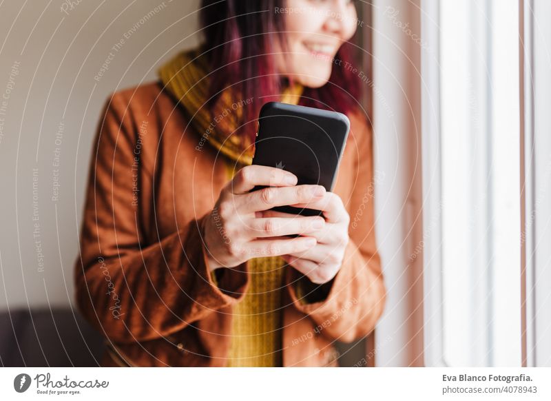 Junge schöne Frau zu Hause mit Handy am Fenster. Technologie und Lebensstil heimwärts Technik & Technologie Heimarbeitsplatz Kaukasier Freizeitkleidung