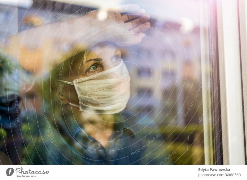 Ältere Frau mit Gesichtsschutzmaske schaut zu Hause aus dem Fenster Menschen Senior reif lässig Kaukasier älter heimwärts alt Alterung häusliches Leben