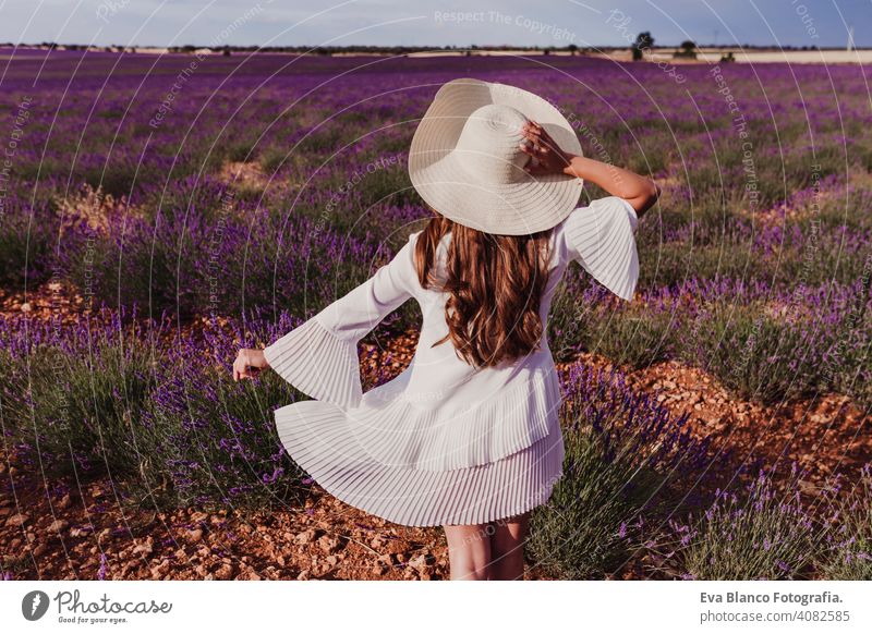 charmante Junge Frau mit einem Hut und weißem Kleid in einem lila Lavendelfeld bei Sonnenuntergang. LIfestyle im Freien. Rückansicht Wiese Schönheit Freude