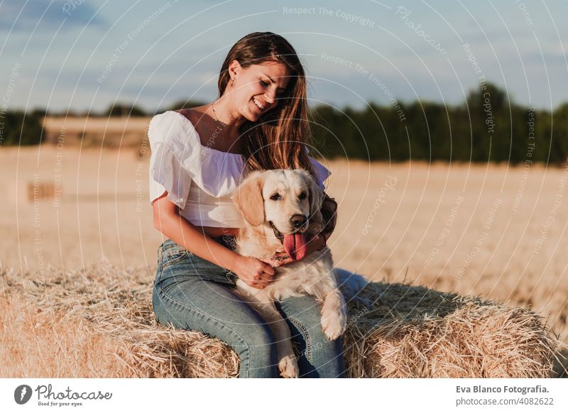 Junge schöne Frau, die mit ihrem Golden Retriever Hund auf einem gelben Feld bei Sonnenuntergang spazieren geht. Natur und Lebensstil im Freien Sommer Mode jung