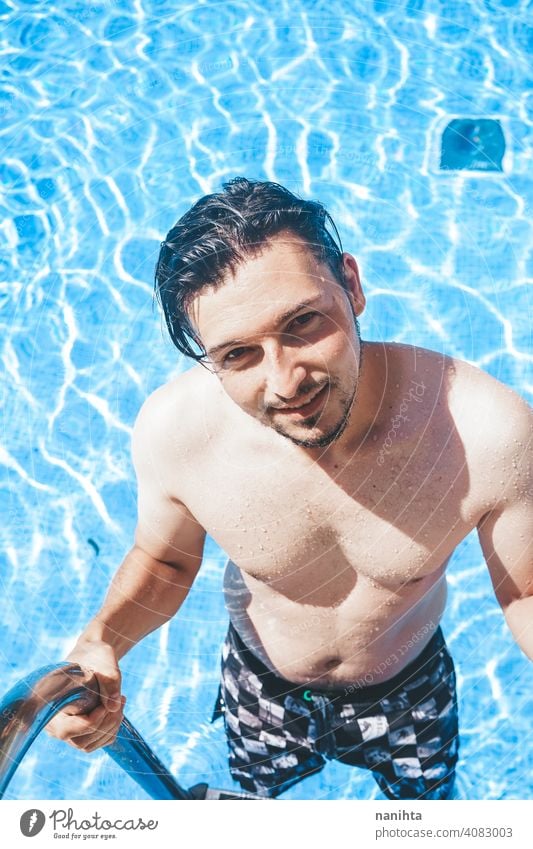 Junger, gutaussehender Mann posiert in der Nähe eines Pools attraktiv sexy männlich Schwimmbad Sommer Haut Vollbart Typ Lächeln Bräune blau Wasser Party Porträt