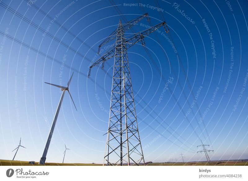 Stromtrasse, Überlandleitung und Windräder, Windkraftanlagen, auf einem Feld, Stromleitungen und Strommast vor blauem Himmel, nachhaltige Stromproduktion und Stromtransport, Weitwinkelaufnahme