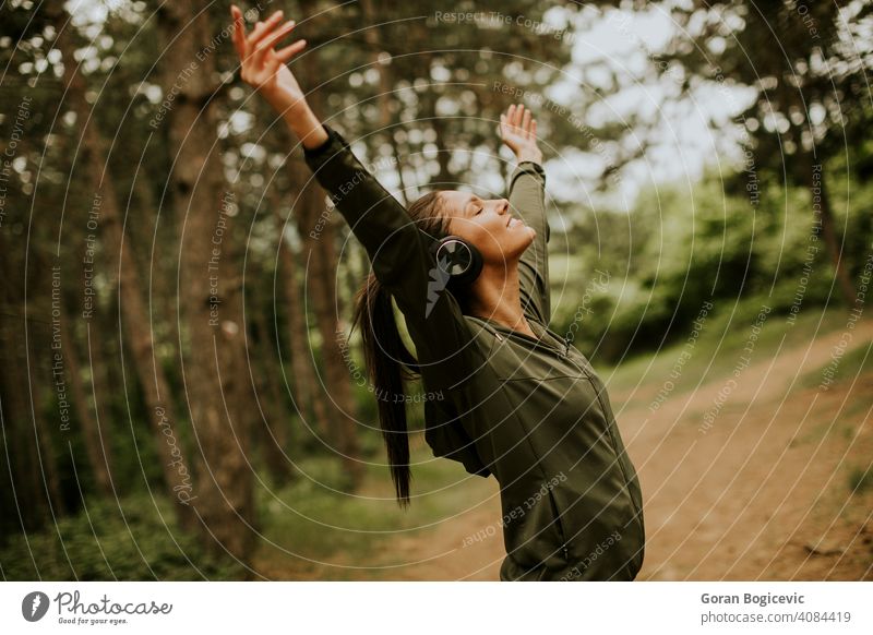 Junge Frau mit Kopfhörern, die ihre Arme im Wald vorhalten, weil sie gerne draußen trainiert Musik hören Lifestyle Kaukasier Fröhlichkeit im Freien Athlet Natur