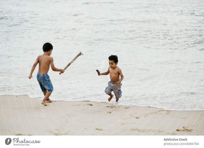 Schwarze Jungen spielen am Strand Brüder MEER Spielen Stöcke Spaß Zusammensein Sommer Wasser ohne Hemd Barfuß Kinder Geschwister Glück Wochenende Lifestyle