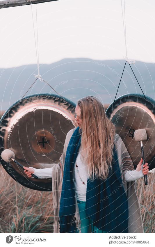 Frau in der Nähe von ethnischen Gongs auf dem Feld Ritual Klang Poloschläger jung Hügel Land Instrument Spiritualität Poncho Kultur Gerät Therapie Energie Musik