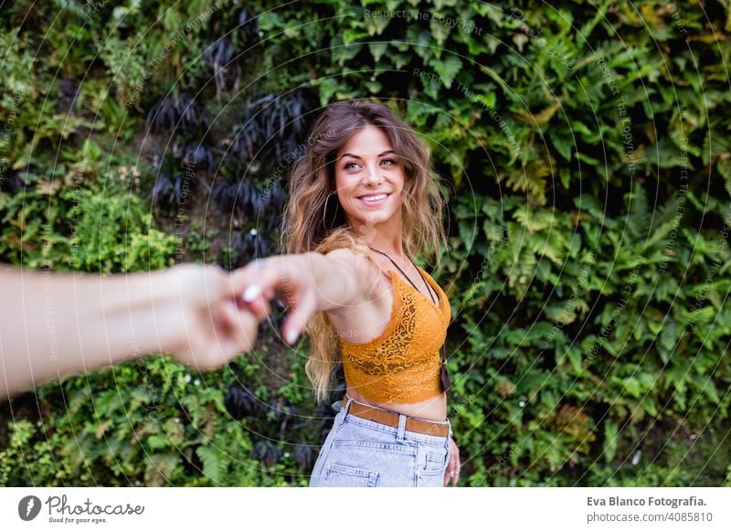 Porträt einer jungen blonden schönen Frau auf der Straße lächelnd. Halten Sie die Hände in einem Follow-Me-Pose. Grüne Vegetation Hintergrund. Lifestyle im Freien. Sommerzeit