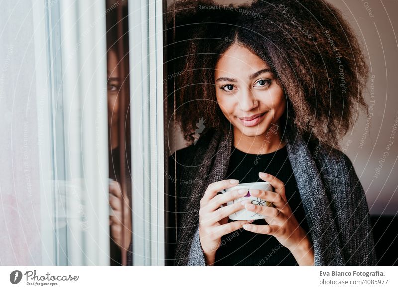 Porträt einer schönen afroamerikanischen jungen Frau am Fenster mit einer Tasse Kaffee in der Hand. Lebensstil im Haus Afroamerikaner heimwärts ethnisch