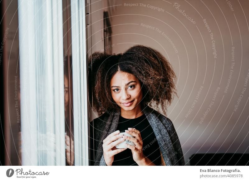 Porträt einer schönen afroamerikanischen jungen Frau am Fenster mit einer Tasse Kaffee in der Hand. Lebensstil im Haus Afroamerikaner heimwärts ethnisch