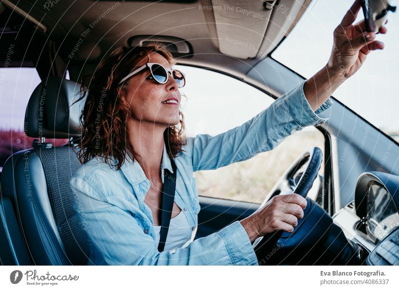 junge schöne Frau, die ein Auto fährt und den Rückspiegel einstellt. Reisekonzept fahren PKW sonnig Sonnenbrille reisen reisend Rad Laufwerk mieten Teilen neu