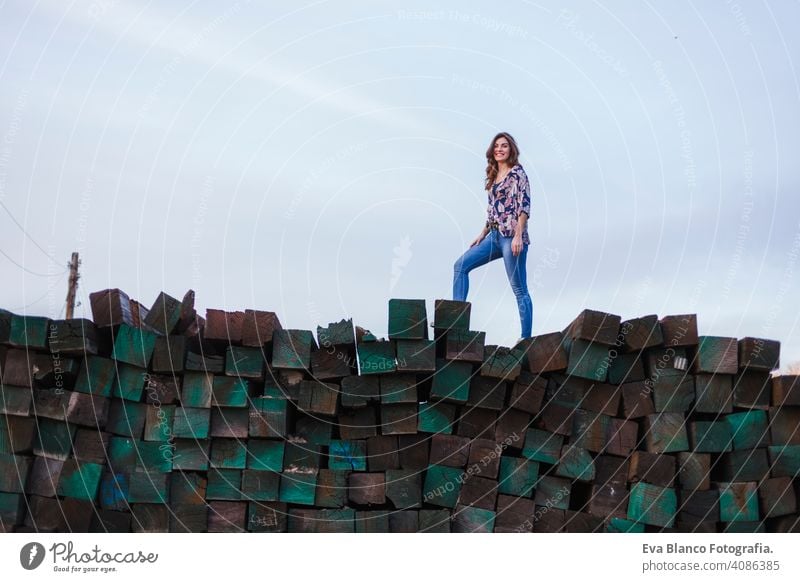 Porträt einer jungen schönen Frau in Freizeitkleidung, die auf einem Berg von grünen Holzblöcken Hintergrund steht und lächelt. Lebensstil im Freien. Jugend