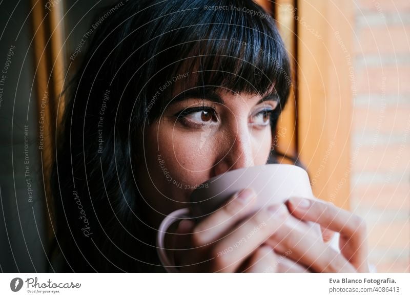 junge kaukasische Frau zu Hause am Fenster mit einer Tasse Kaffee oder Tee. Morgen und entspannen Konzept. Lebensstil im Innenbereich Mädchen bequem