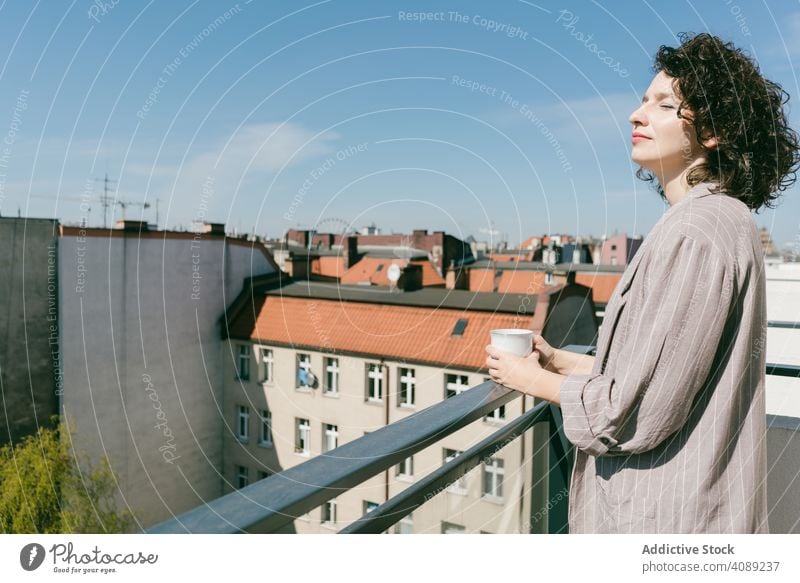 Elegante Frau genießt die Sonne auf der Terrasse Balkon Tasse Kaffee Reling Lehnen geschlossene Augen genießend Sonnenlicht entspannt jung Freude heiter schön