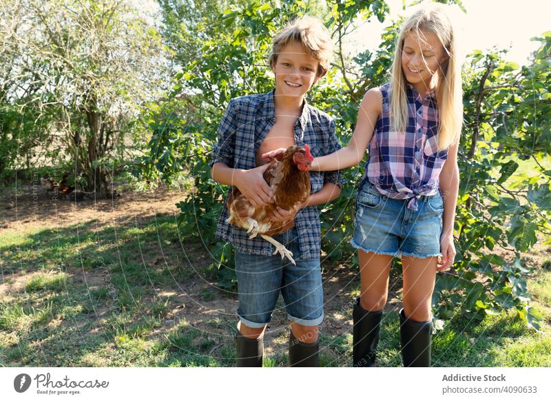 Fröhliche Geschwister mit Huhn auf dem Bauernhof Hähnchen Lächeln Streicheln Teenager Sträucher sonnig tagsüber Zusammensein Schwester Bruder Mädchen Junge Tier