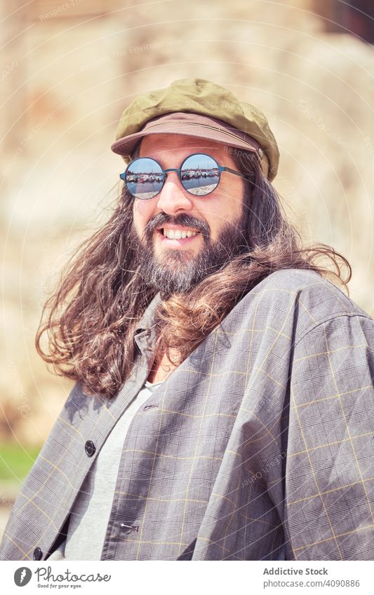 stilvollen bärtigen Mann mit langen Haaren sitzen auf der Straße mit Sonnenbrille trendy Schnurrbart Porträt Typ Blick Behaarung cool stylisch gutaussehend