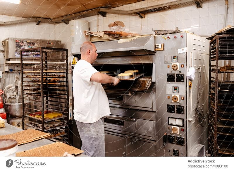 Männlicher Bäcker schiebt Kuchen in den Ofen Mann Bäckerei Konditor setzen heiß roh Arbeit Dessert Gebäck männlich Erwachsener erwärmen professionell