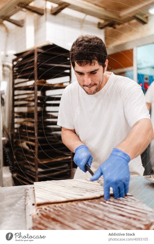 Anonymer Koch schneidet Kuchen auf dem Tisch an Konditor Bäckerei geschnitten Messer Gebäck süß frisch Küche Lebensmittel Vorbereitung Kleinunternehmen Mann